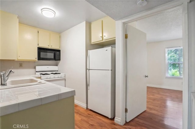 kitchen with sink, white appliances, tile counters, and light wood-type flooring