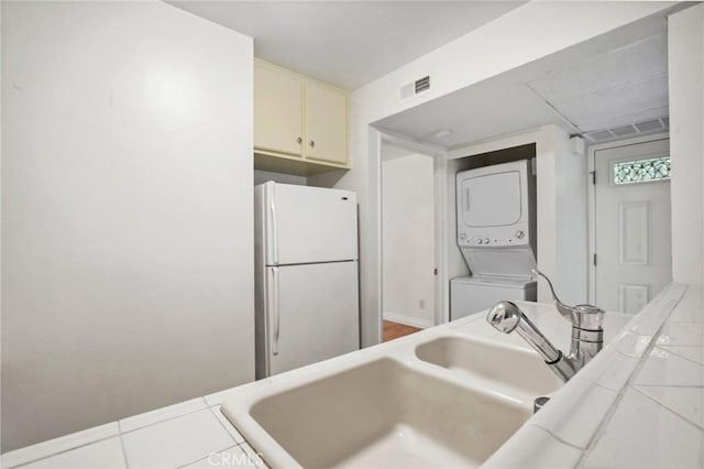 kitchen featuring stacked washer and dryer, sink, white refrigerator, cream cabinets, and tile counters