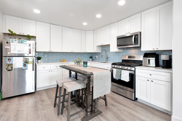 kitchen with sink, a breakfast bar area, white cabinetry, light hardwood / wood-style flooring, and stainless steel appliances