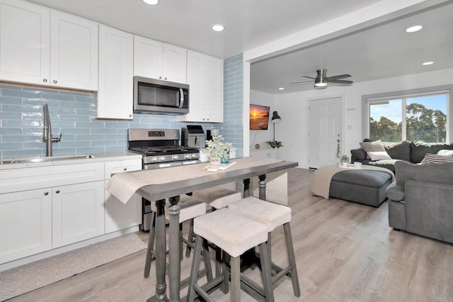 kitchen with sink, tasteful backsplash, light hardwood / wood-style flooring, stainless steel appliances, and white cabinets