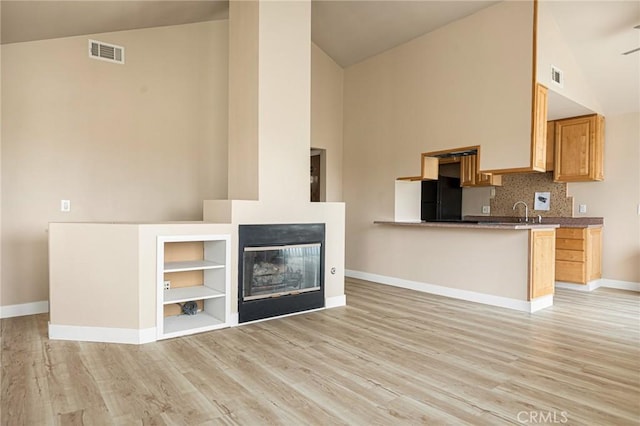 kitchen featuring black refrigerator, light hardwood / wood-style flooring, high vaulted ceiling, and kitchen peninsula