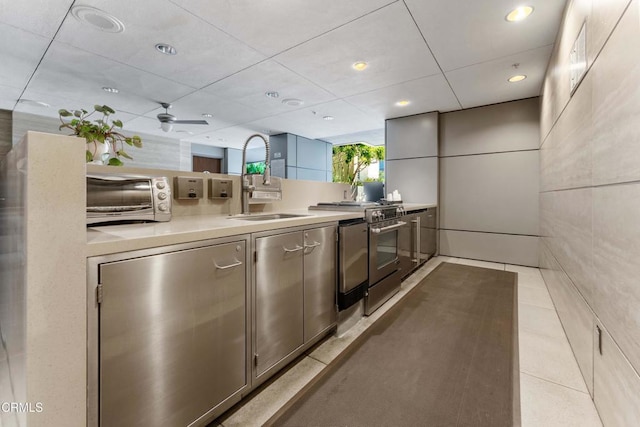 kitchen featuring light tile patterned flooring, stainless steel stove, sink, gray cabinetry, and tile walls