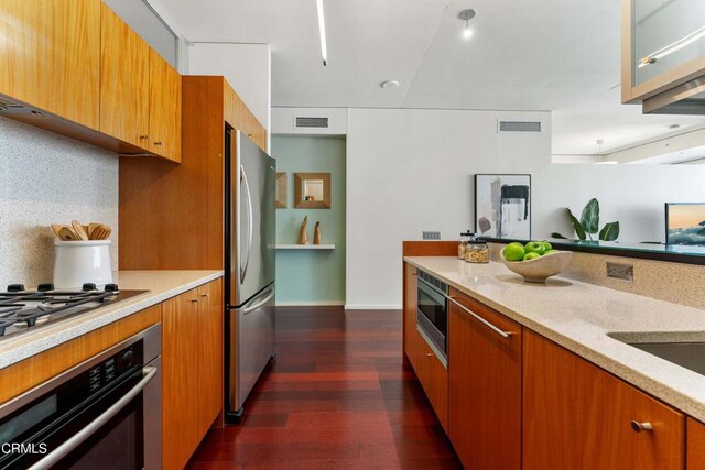 kitchen featuring light stone counters, decorative backsplash, dark wood-type flooring, and appliances with stainless steel finishes