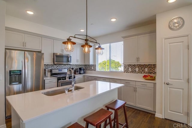 kitchen with sink, tasteful backsplash, decorative light fixtures, an island with sink, and stainless steel appliances