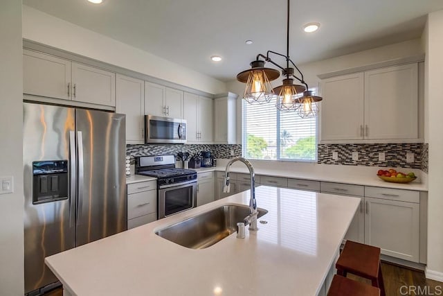 kitchen featuring sink, a kitchen island with sink, hanging light fixtures, stainless steel appliances, and tasteful backsplash