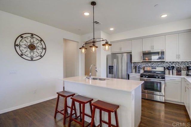 kitchen with decorative light fixtures, sink, backsplash, a kitchen island with sink, and stainless steel appliances