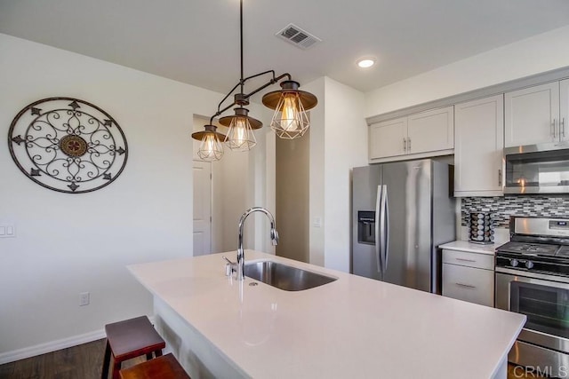 kitchen with appliances with stainless steel finishes, sink, backsplash, hanging light fixtures, and a kitchen island with sink