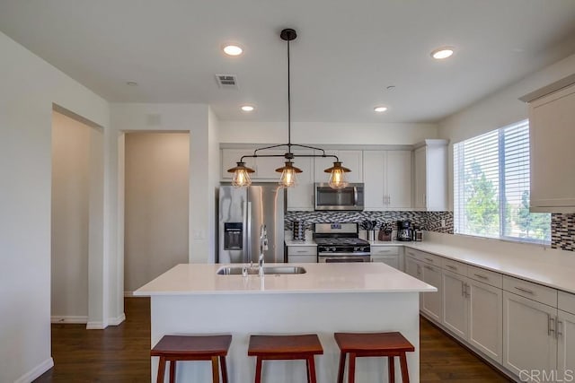 kitchen featuring sink, a center island with sink, appliances with stainless steel finishes, pendant lighting, and backsplash