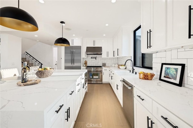 kitchen with pendant lighting, white cabinetry, high quality appliances, and light stone counters