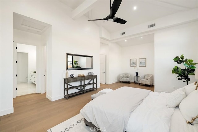 bedroom featuring beam ceiling, light hardwood / wood-style flooring, and a towering ceiling