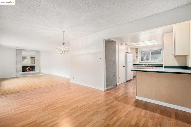 kitchen featuring an inviting chandelier, a brick fireplace, a textured ceiling, light hardwood / wood-style flooring, and white fridge