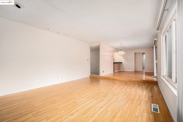 unfurnished living room featuring a wealth of natural light, an inviting chandelier, a textured ceiling, and light hardwood / wood-style flooring