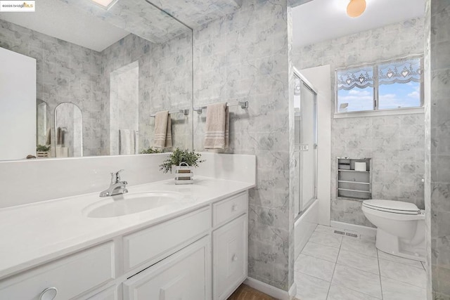 full bathroom with tile walls, shower / bath combination with glass door, tile patterned flooring, vanity, and toilet