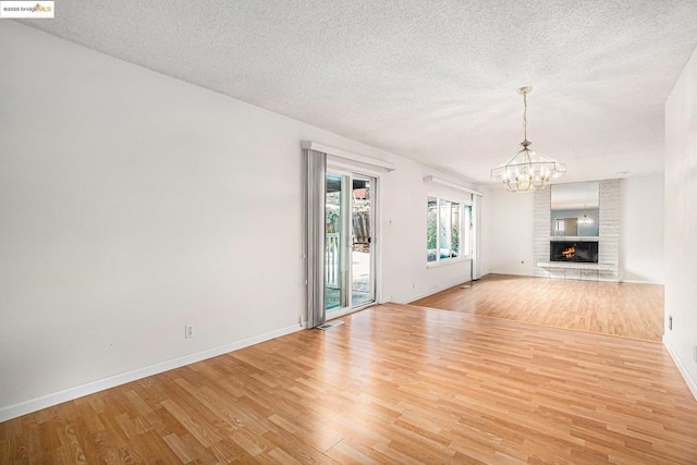 unfurnished living room featuring an inviting chandelier, a fireplace, light hardwood / wood-style flooring, and a textured ceiling