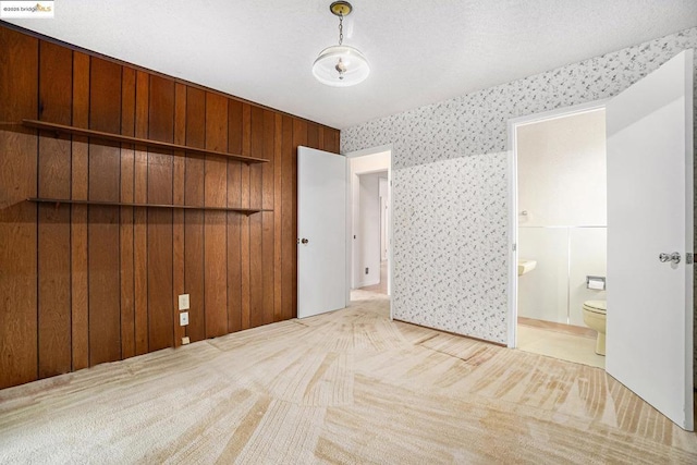 unfurnished bedroom with ensuite bathroom, light colored carpet, and wooden walls