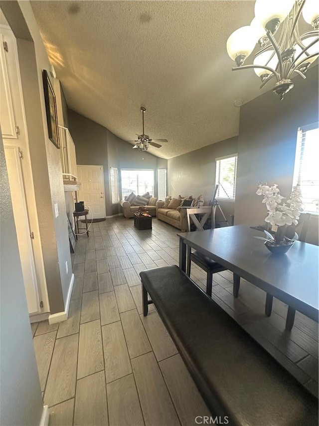 dining space featuring lofted ceiling, a healthy amount of sunlight, ceiling fan with notable chandelier, and a textured ceiling