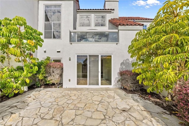 rear view of property with a patio, a chimney, a tile roof, and stucco siding