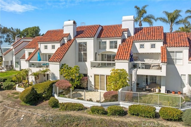 rear view of property with a tile roof, a chimney, a residential view, fence, and stucco siding