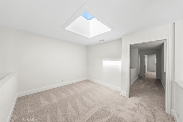 empty room featuring a skylight, light carpet, and baseboards