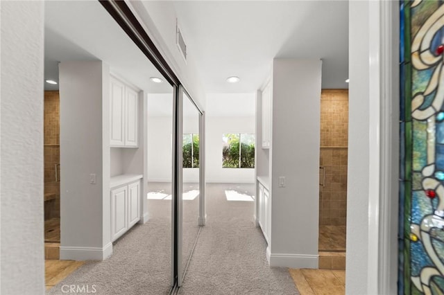 hallway with baseboards and light colored carpet