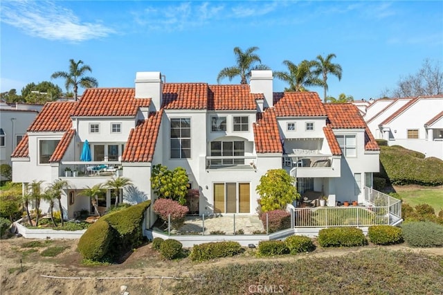 back of property with a chimney, stucco siding, a balcony, a residential view, and a tiled roof