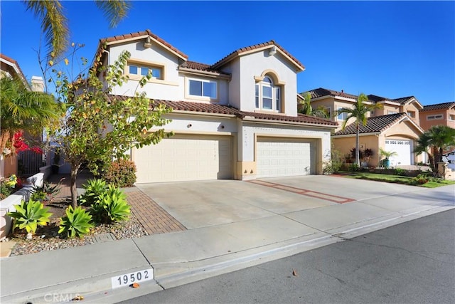 mediterranean / spanish house with driveway, a tiled roof, an attached garage, and stucco siding