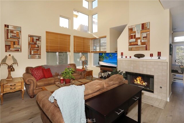 living room with a tile fireplace, a towering ceiling, and light wood-type flooring