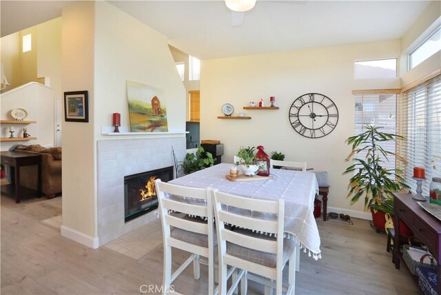 dining space with a tiled fireplace, a high ceiling, and light wood-type flooring