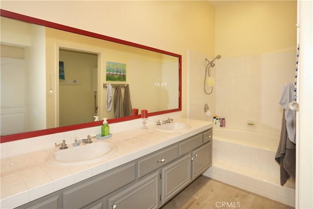 bathroom with double vanity, tiled shower / bath, a sink, and wood finished floors