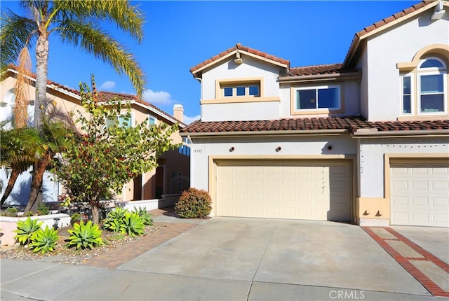 mediterranean / spanish house with a garage, driveway, a tiled roof, and stucco siding