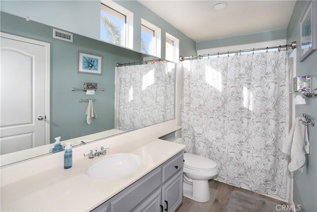 bathroom featuring visible vents, a shower with shower curtain, toilet, wood finished floors, and vanity