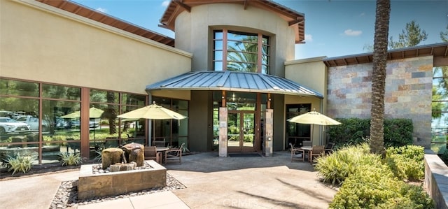 view of exterior entry featuring metal roof, a standing seam roof, a patio area, and stucco siding