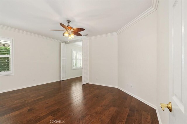 spare room featuring baseboards, ornamental molding, dark wood-type flooring, and a wealth of natural light