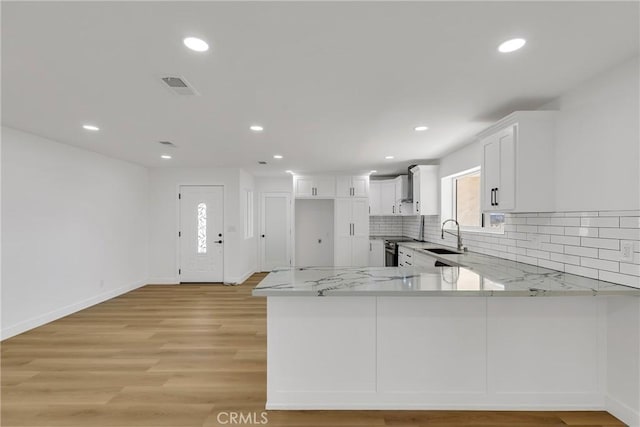 kitchen featuring sink, white cabinetry, light stone counters, kitchen peninsula, and light wood-type flooring