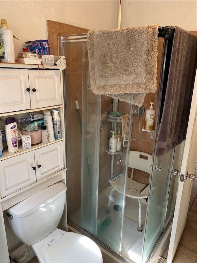 bathroom featuring toilet, tile patterned floors, and a shower with shower door