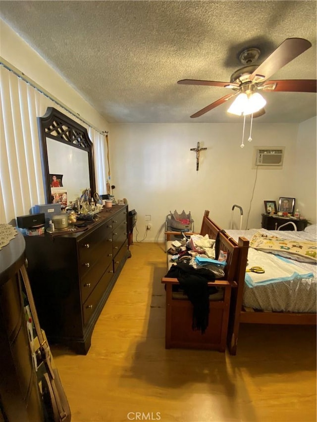 bedroom with ceiling fan, a wall unit AC, a textured ceiling, and light wood-type flooring