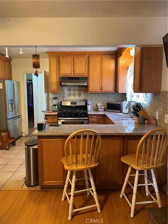 kitchen featuring a kitchen bar, sink, decorative light fixtures, kitchen peninsula, and stainless steel appliances