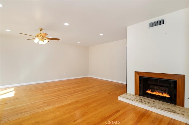 unfurnished living room featuring light wood-style floors, a warm lit fireplace, visible vents, and baseboards