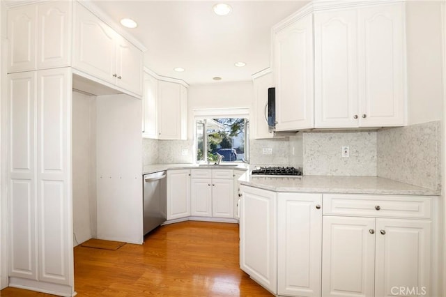 kitchen with light stone counters, stainless steel appliances, a sink, white cabinetry, and light wood finished floors