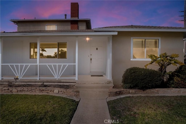 doorway to property with a yard, a chimney, and stucco siding