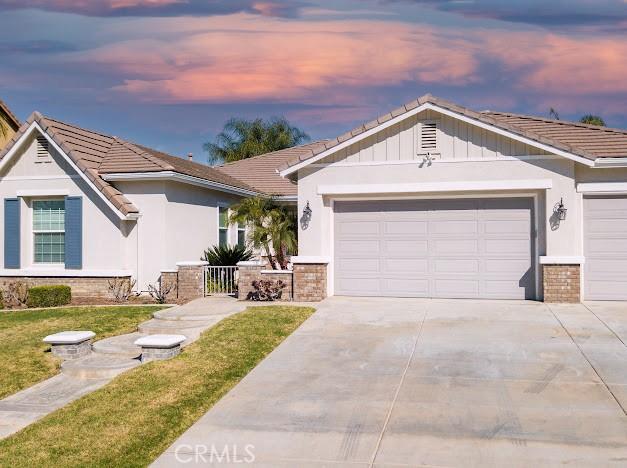 ranch-style house with a garage, driveway, a tile roof, and stucco siding