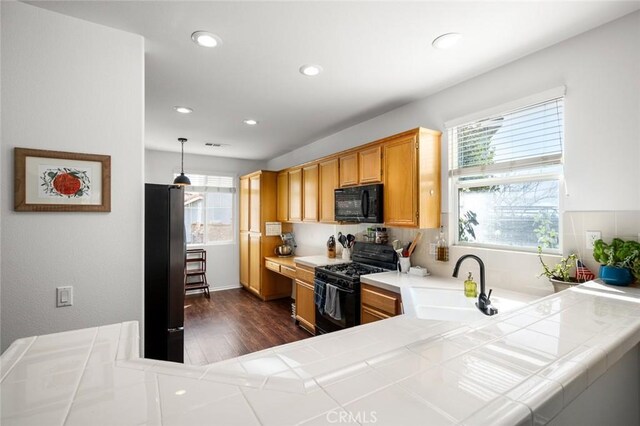 kitchen featuring sink, hanging light fixtures, tile counters, black appliances, and dark hardwood / wood-style flooring