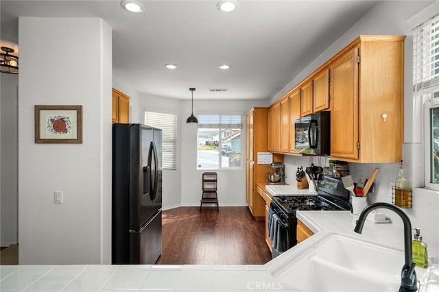 kitchen with dark wood-type flooring, sink, tile countertops, hanging light fixtures, and black appliances