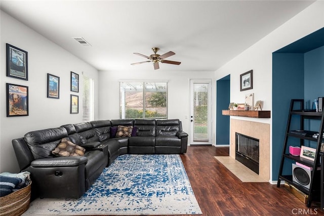 living room featuring a tiled fireplace, dark wood-type flooring, and ceiling fan