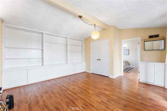 unfurnished living room featuring wood-type flooring, vaulted ceiling with beams, and a textured ceiling