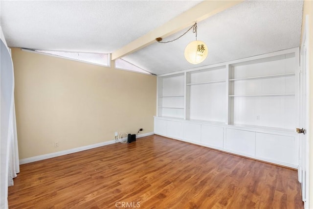 empty room featuring hardwood / wood-style flooring, vaulted ceiling with beams, built in features, and a textured ceiling