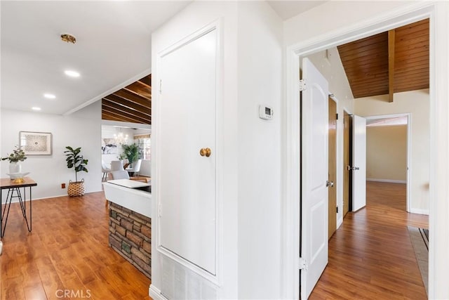 corridor featuring lofted ceiling with beams, wood-type flooring, and a notable chandelier