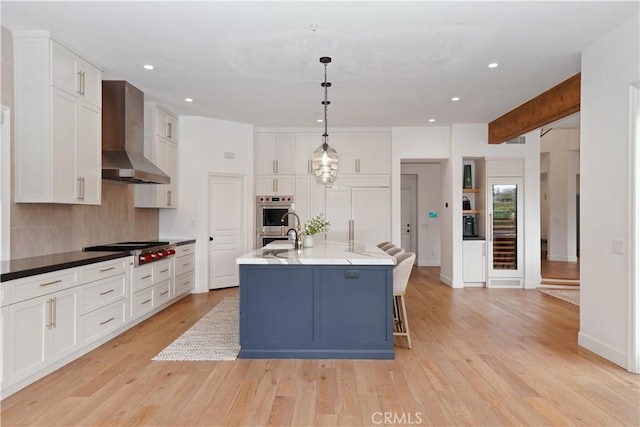 kitchen with backsplash, light wood-style flooring, white cabinets, stainless steel appliances, and wall chimney exhaust hood