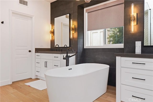 bathroom with visible vents, a freestanding bath, vanity, wood finished floors, and tile walls