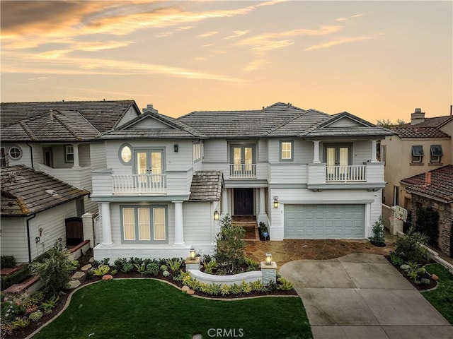 view of front of house with a garage, a balcony, a yard, and french doors